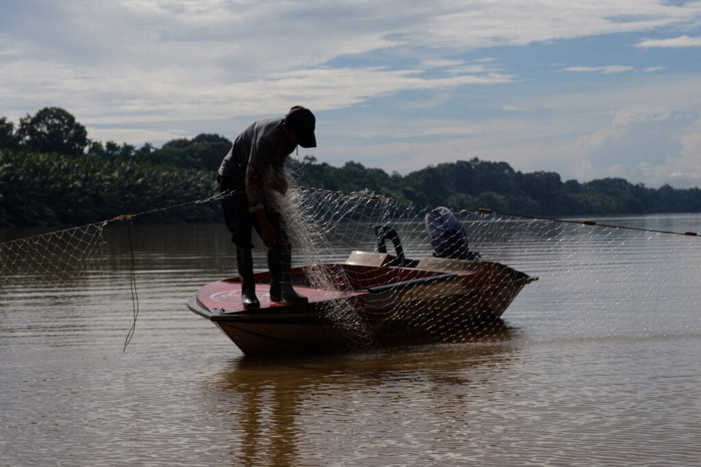 A fisherman examines a hole in his net.